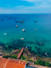 Fototapeta premium Aerial View of Clear Turquoise Ocean with Tourist Speedboats and Fishing Vessels Anchored near a Rocky Shore