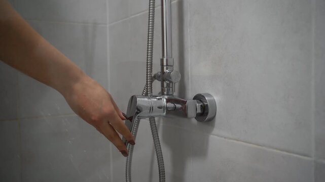 Hygiene concept. female hand turn on shower faucet in bathroom interior