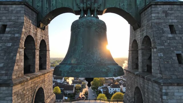 Large bronze bell in a stone cathedral tower at sunset. Historic church architecture overlooking a small town. Aerial view of a green patina bell