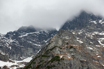Tatra Mountains in Poland featuring rocky peaks, snow-covered slopes, and low-hanging clouds creating a dramatic alpine landscape