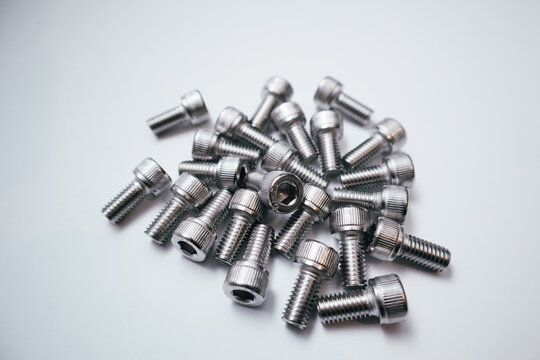 Pile of stainless steel socket head cap screws on a white background.