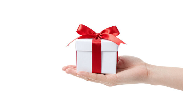 Hand presents a small white gift box tied with a vibrant red ribbon, isolated on white background