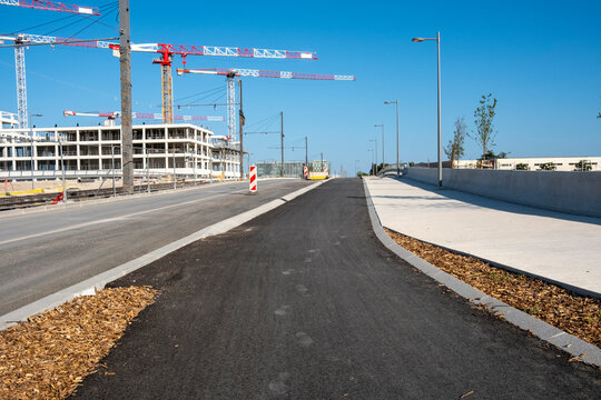 Empty urban road with asphalt sidewalk and horizon showing construction cranes and development under wide sky creating future city copy space background