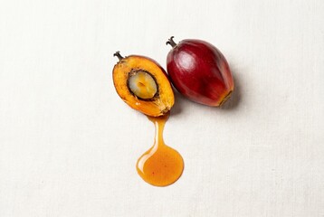 Naklejka premium Fresh red oil palm fruit cut in half with oil dripping onto white fabric background top view