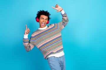Young man wearing a colorful sweater dancing with headphones against a blue background