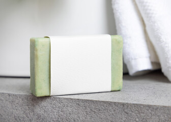 Green soap bar with blank label near white bath towels and basin on grey stone, mockup