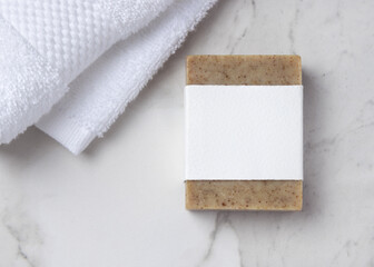 Mockup of brown solid soap bar with blank paper label near white bath towel on marble, personal care