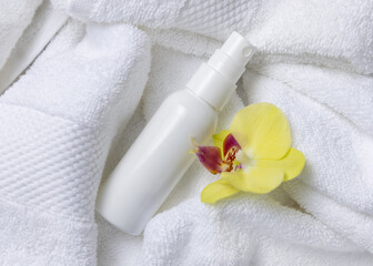 Mockup of white blank spray cosmetic bottle with yellow orchid flower on bath towel