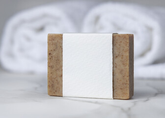 Mockup of brown solid soap bar with blank paper label near white bath towel, personal care packaging