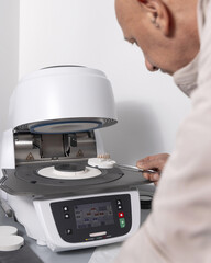 Orthodont men puts tooth implants into dental ceramic oven for baking enamel. Dental prosthetics