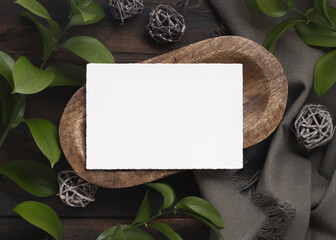 Horizontal card mockup on brown wooden tray near green leaves and grey fabric  top view