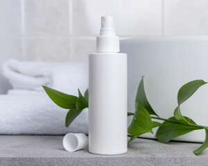 White blank cream bottle near green leaves, basin and white bath towels on grey stone, mockup