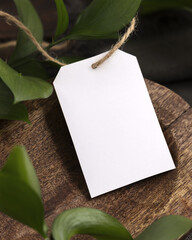 Vertical gift tag mockup on brown wooden tray near green leaves and grey fabric closeup