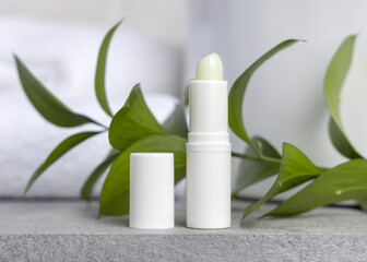 White blank cream tube against green leaves on grey stone in white bathroom, mockup