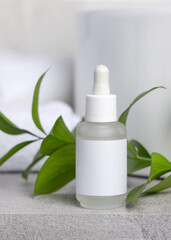 Mockup of dropper bottle with a label against green leaves on grey, Spa and beauty treatments