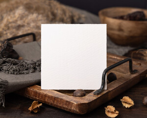 Square card on wooden tray near brown decor and grey linen cloth closeup, boho mockup