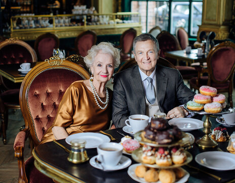 Starsza kobieta w perłach i jedwabiu i towarzyszący jej elegancki mężczyzna celebrują Tłusty Czwartek w luksusowej restauracji