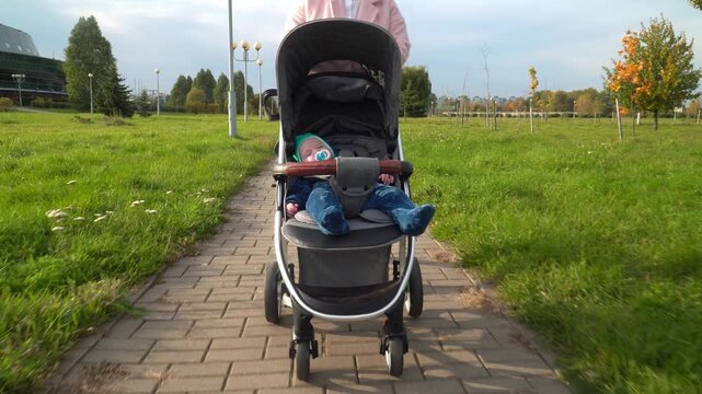 baby in stroller being pushed along paved park path near modern building, capturing a peaceful moment of outdoor childcare, urban nature, and early childhood