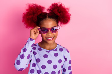 Playful young girl with pink sunglass and purple polka dot shirt smiles against a bright pink backdrop © deagreez