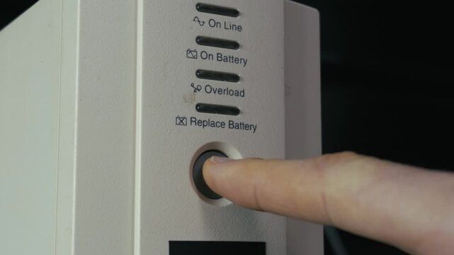 Close-up of a finger pressing the power button on a white UPS device to illuminate the amber light. Concept of energy security, backup power solutions, and electrical safety.
