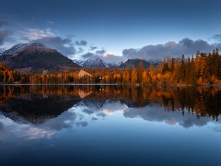Fototapeta premium Strbske Lake, Slovakia - Reflecting iconic Strbske Lake (Strbske Pleso) on a sunny autumn afternoon with High Tatras and Tatras Tower at background. Warm autumn colors Tatras mountains with clouds