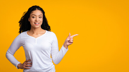 A young woman with curly hair smiles and points to the side. She wears a white long-sleeve shirt...