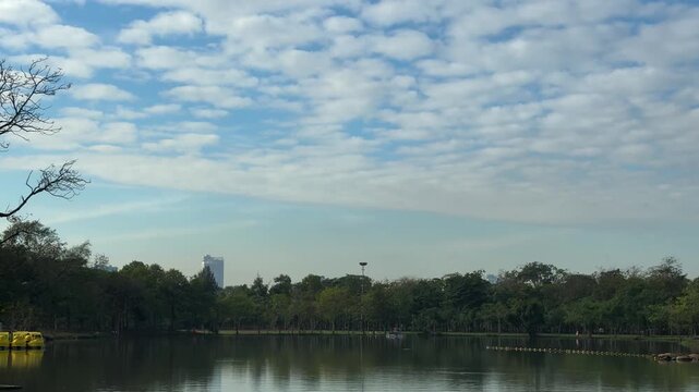 Early morning light bathes a wide, calm lake that reflects a tree-lined shore beneath a broad, partly cloudy sky. 