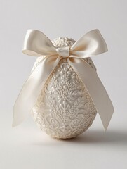 A beautifully detailed white egg with a large satin bow on top. The ornate egg displays delicate floral motifs with a flowing satin ribbon on a light surface.