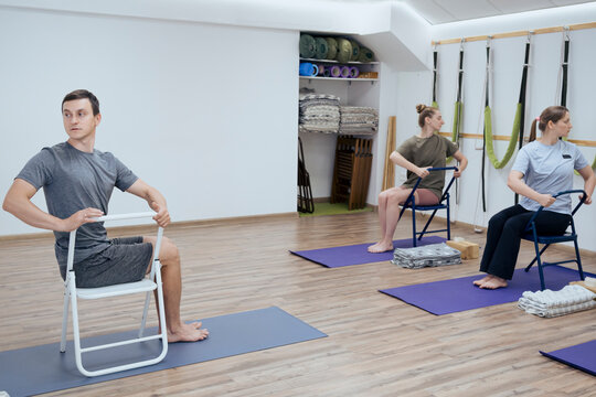 Group of people doing seated spinal twist yoga asana with chair indoor