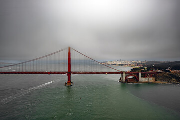 Obraz premium Aerial view of the Golden Gate Bridge 🌉 spanning the Pacific entrance to San Francisco Bay, with one tower disappearing into thick grey fog above the deep green water.