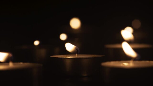Close up of burning candles with warm yellow flames glowing in darkness