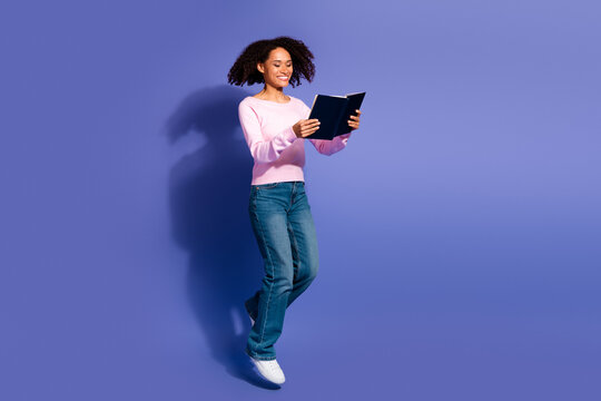 Young woman floats against a violet background reading a book with a bright smile casual stylish moment