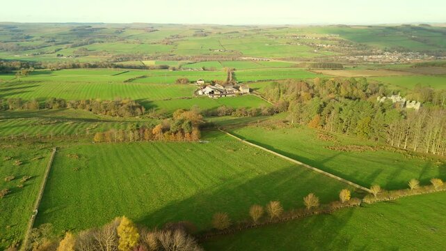 A drone captures a view of green fields in Northumberland near Hexham. The landscape features trees and a farmhouse in the distance under a clear sky