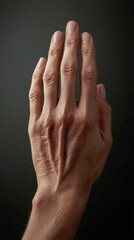 A hand with visible wrinkles and short nails is shown. The hands detailed skin texture and short nails are prominently displayed against dark backdrop.