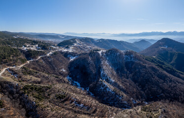 Obraz premium Expansive mountain landscape with a winding road and patches of snow under a clear blue sky
