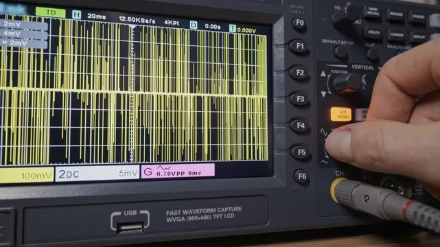 Close-up of an engineer's hand adjusting a knob on a digital oscilloscope to calibrate a signal waveform. Concept of electronic diagnostics, scientific research, and data analysis.