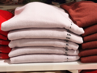 size range. Colour range. showcase stack of sweaters in the store . multi-colored knitted sweaters stacked in piles on a wooden counter in a clothing store.