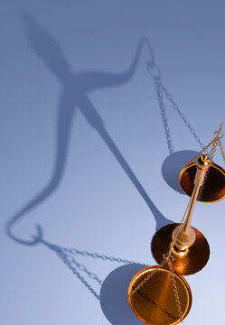 A close-up, high-angle view of a gleaming golden justice scale with its distinctive shadow stretching across a smooth blue surface, representing fairness and equilibrium