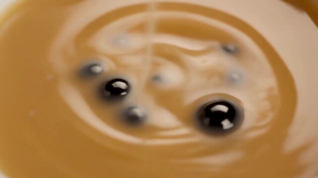Close-up of black tapioca pearls sinking into creamy milk tea with a slow swirl, 4K loop