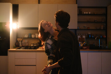 Romantic couple sharing a joyful moment in a cozy kitchen at night with warm lighting © arthurhidden