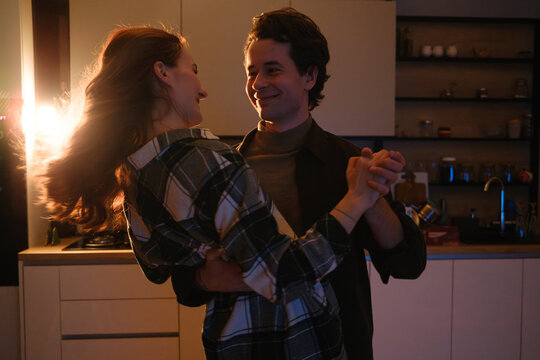 Couple dancing in a warmly lit kitchen at night sharing a joyful and intimate moment