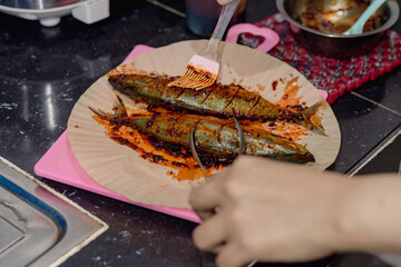A woman using a brush to apply seasoning to mackerel before cooking