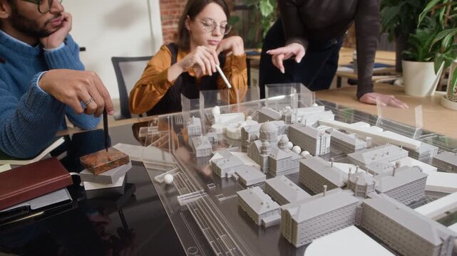Tilt up of diverse group of architects collaborating and reviewing 3D layout on table in bright, modern architectural office with open workspace and contemporary design