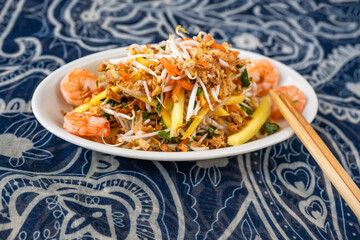 Fresh mango salad with shrimp and chopstick on ornamental blue white background.