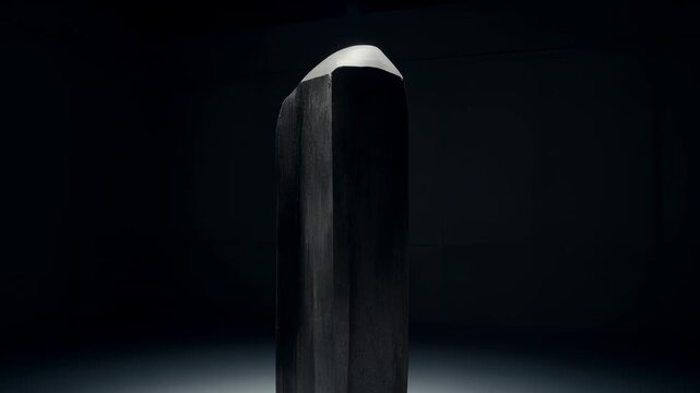 Dollying camera revealing monolithic sculpture in gallery under spotlight, highlighting faceted top