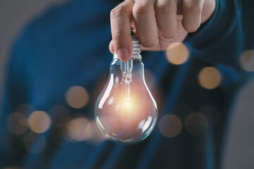 Hand holding glowing light bulb with warm light inside, symbol of new idea, inspiration, creativity innovation, representing potential, beginning, future opportunity for business and personal growth. © Bordinthorn