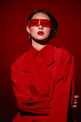 Young woman wearing a bold red outfit and translucent red sunglasses looks confidently at the...