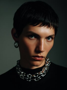 Close-up portrait of a young woman's face. she has short, dark hair that is styled in a pixie cut with bangs. her eyes are looking directly at the camera with a serious expression.