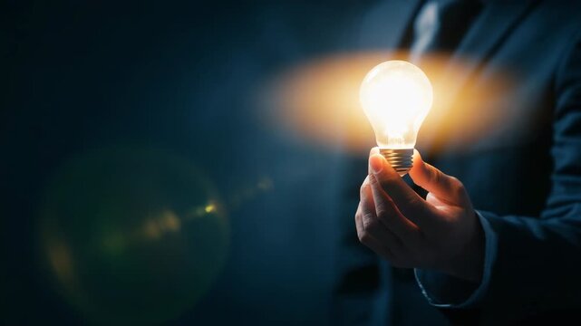Businessman holding a glowing light bulb on his palm, concept of creative idea, innovation, inspiration, and business solution in dark background.