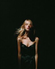 Naklejka premium Sensual Woman in Evening Dress Posing in Dramatic Light, Dark Backdrop